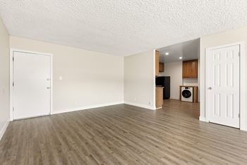 An empty living room with wood flooring and a kitchen